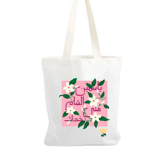 White tote bag with pink floral design and Arabic text on a white background